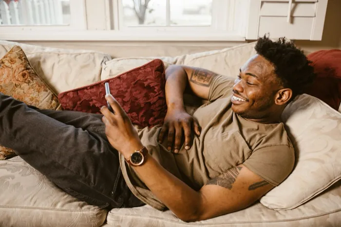 A young man on a couch, smiling at his phone.