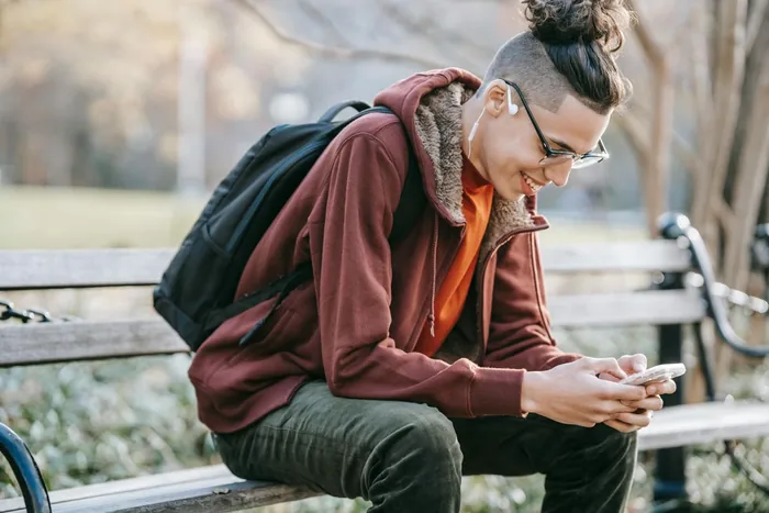 A young man on a park bench, smiling at his phone.