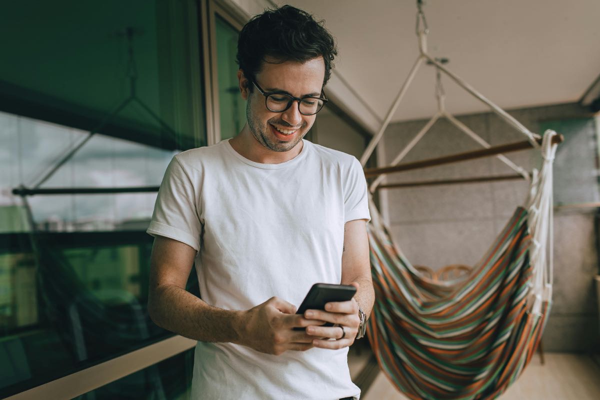 A man on a balcony reading a message on his phone.
