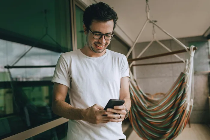 A man on a balcony reading a message on his phone.