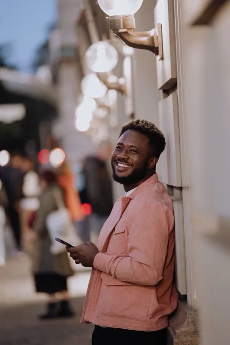 A man smiling at his phone on an evening street, warmly lit.